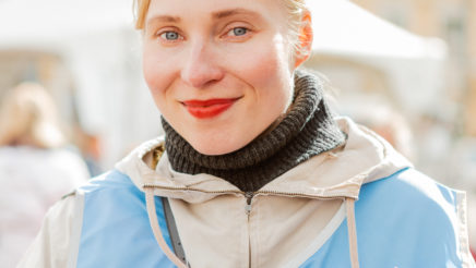 Vaaleatukkainen nainen seisoo valoisalla torilla ja pitelee kasaa Martat -lehtiä. Hänellä on valkoisen takin päällä vaaleansininen Martat -liivi.