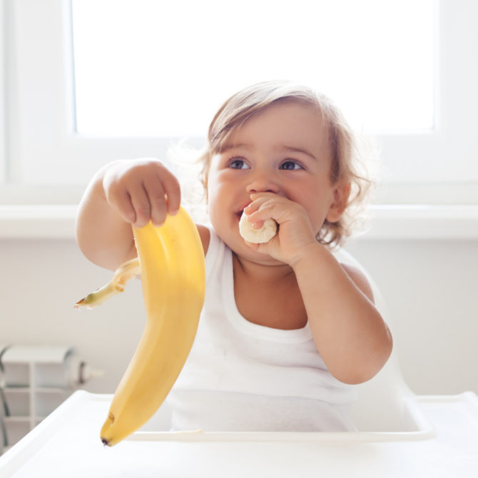 Vauva istuu syöttötuolissa ja pitelee kädessään banaaninkuorta. Hän työntää suuhunsa banaaninpalaa.