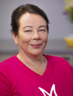 Mustahiuksinen nainen pinkissä Martta teepaidassa. Tausta on harmaa.