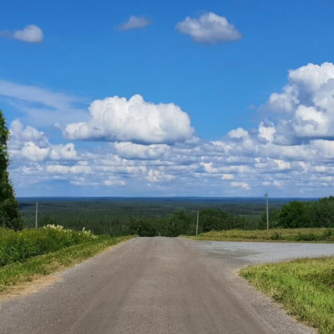 Tie joka jatkuu pitkälle, pilviä taivaalla ja horisontissa metsä