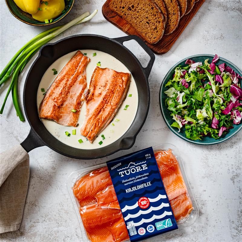 Paistinpannu, jossa kalaa, ympärillä myös muita ruokatuotteita sekä Saimaan Tuoreen myyntipakkaus. 